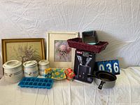Overview of lot showing coffee grinder box, canisters, basket with loaf pans, framed art, saucepan, ice tray, and placard