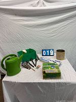 All items in lot displayed: watering can, edging box, solar lights, bin, planter pot, hose fitting