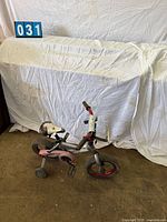 Full view of toddler bike showing overall condition, training wheels, red rims