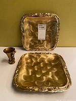 Two square brass trays and one flared brass candle holder displayed together