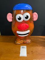 Front view of translucent orange Mr. Potato Head container with lot tag visible