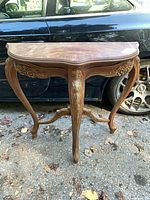 Full front view of carved wood table showing three legs, carvings, surface wear