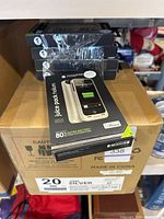 Five retail boxes visible stacked, each box labeled to contain 20 Mophie Juice Pack Helium cases. One retail box is taken out and visible on top in front, showing sealed packaging.