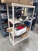 Full view of beige 4-tier plastic shelving unit loaded with items, showing overall structure and shelving design.