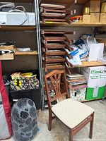 Side view of a wooden dining chair with a beige upholstered seat and carved backrest, surrounded by storage items.
