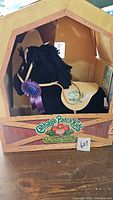 Front view of the black Cabbage Patch Kids Show Pony in cardboard display box with saddle, purple ribbon, and Cabbage Patch Kids Show Pony logo on box.