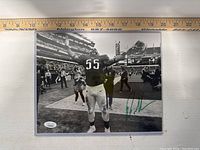 Full view of the signed 8x10 photo showing Brandon Graham on a football field with arms raised and the autograph visible in green ink.