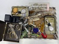 Overall view of the mixed items in a box including watches, flatware utensils, keychains, jewelry pieces, and a small whistle.