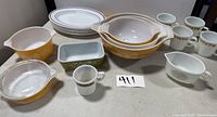 Photo showing overall grouping including Pyrex netting pattern bowls and casserole dish, white mugs, and plates