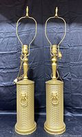 Pair of vintage gold painted metal lamps without shades shown from front on a dark background.