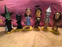 Photo showing the full set of six Wizard of Oz bobbleheads on yellow brick bases, from Wicked Witch on the left to Cowardly Lion on the right.