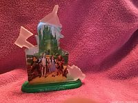 Photo showing Bradford Exchange Wizard of Oz collectible sculpture with characters and Emerald City in front of a pink textured background.