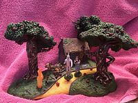 Wide view of the Wizard of Oz Hawthorne Village set showing Tin Man's house, two large apple trees with apples, and figurines of the Tin Man and other characters on a yellow brick road base.