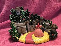 Photo of miniature fantasy village set featuring thatched roof houses, yellow brick road, green landscaping, and figurines of female and male characters.