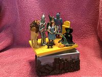 Photo showing the Westland Wizard of Oz jewelry box with characters Dorothy, Tin Man, Scarecrow, Cowardly Lion, and melting Wicked Witch on a yellow platform and decorated base.
