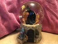 Front view of the Wicked Witch inside clear glass water globe on stone wall themed base with a monkey figurine and basket