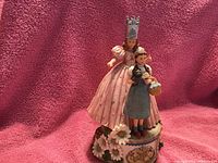 Photo of the San Francisco Music Box showing Dorothy in blue dress holding a basket and Glinda in a pink gown with crown, standing on a floral decorated base with Wizard of Oz logo.