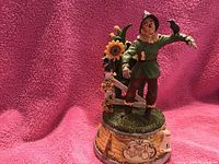 Photo showing the Scarecrow figurine standing on a decorated music box base with a pink background.