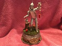 Tin Man music box figurine on a decorative circular base with 'The Wizard of Oz' plaque, holding a heart pendant chain.