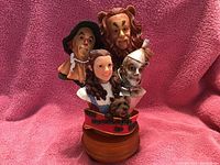 Front view of the Wizard of Oz music box featuring four character busts including the Scarecrow, Dorothy, Tin Man, and Cowardly Lion placed on a wooden music box base.