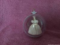 Close-up of a Hallmark Christmas ornament showing Glinda the Good Witch figurine inside clear spherical globe with star-shaped hanging topper.