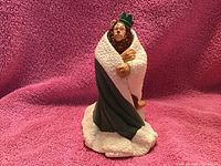 Photo of the Hallmark Christmas ornament showing the Cowardly Lion character in a robe standing on a snow base against a pink backdrop.