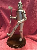 Photo of a 15-inch tall Tin Man figurine with metallic silver finish and wooden base inscribed 'To Oz!'