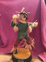 Full view of the 22-inch tall cloth Scarecrow figurine from Wizard of Oz standing on a yellow brick road base, with detailed cloth patchwork and straw stuffing.