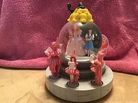 Photo of the Westland Munchkin Lullaby Girls Wizard of Oz snow globe featuring Dorothy and Glinda inside the globe and four pink-clad Munchkin girls arranged around the base.
