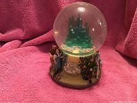 Photo of the Wizard of Oz snow globe showing Emerald City inside the globe and character figurines including Dorothy with Toto, Scarecrow, Tin Man, and Cowardly Lion around the base.