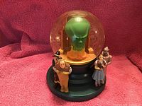 Front view of Wizard of Oz snow globe with four characters and green Wizard figure inside clear globe