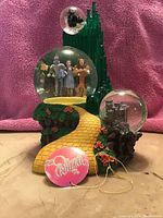 Front view of the green Emerald City music box with three water globes containing Wizard of Oz characters and scenes, and a yellow brick road leading up to the central globe.