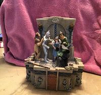 Photo showing San Francisco music box themed on the Wizard of Oz, featuring five key characters standing on a detailed castle base, against a pink backdrop.