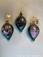 Three Wizard of Oz Christmas ornaments with detailed character images hanging side by side.