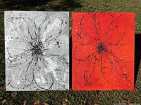 Two paintings side by side on grass, one grey and white with black floral splatter design, the other red with black floral splatter design.