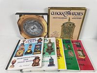 Seven clocks and watches reference books arranged upright on a white surface, showing colorful covers with images of antique and classic clocks and watches.