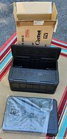 Two black packable foldable insulated cooler chill chests with one open showing interior and an open cardboard box behind them.