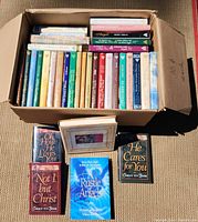 Overhead view of a box filled with multiple religious books arranged in two rows. Includes a variety of hardcover and paperback volumes. Titles and authors are visible on many spines including multiple works by Corrie ten Boom.