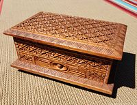 Side and drawer view of the wooden box showing detailed carved floral and geometric designs and the drawer pulled out revealing removed inner compartment.