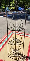 Full view of corner metal plant stand showing four shelves and decorative scrolls in black metal.