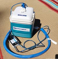 Full view of the PolarCare 300 main unit with power cord, blue insulated tubing, and knee cooling pad attached.