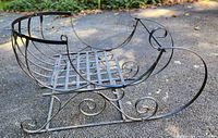 Side angle view of large metal decorative sleigh showing scroll design and lattice seat