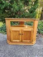 Front view of light wood corner TV stand with two-door cabinet and open shelf.