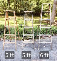 Photo shows three wooden step ladders standing outdoors side by side. Ladders measure 5 feet, 5 feet, and 6 feet respectively.