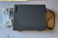 Closed view of the carrying case and included accessories (lift-off correction cassette, cleaner) alongside the power cord.