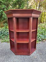 Front view of trapezoid-shaped wooden display shelf featuring 3 shelves and a dark reddish-brown finish.