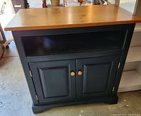 Front view of the wood TV stand cabinet showing the honey pine top and green base with two cabinet doors and open shelf.