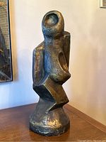 Full view of front side showing the abstract head and torso of the sculpture, painted gold with some wear.