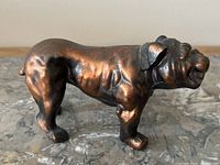 Side view of the copper English Bulldog figurine on a marble-like surface, showing the muscular build and patina.