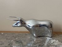 Side view of polished pewter bull sculpture with curved horns, reflecting the surroundings on its smooth surface.